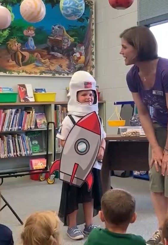 An educator talks with a young child dressed as an astronaut on a rocket ship.