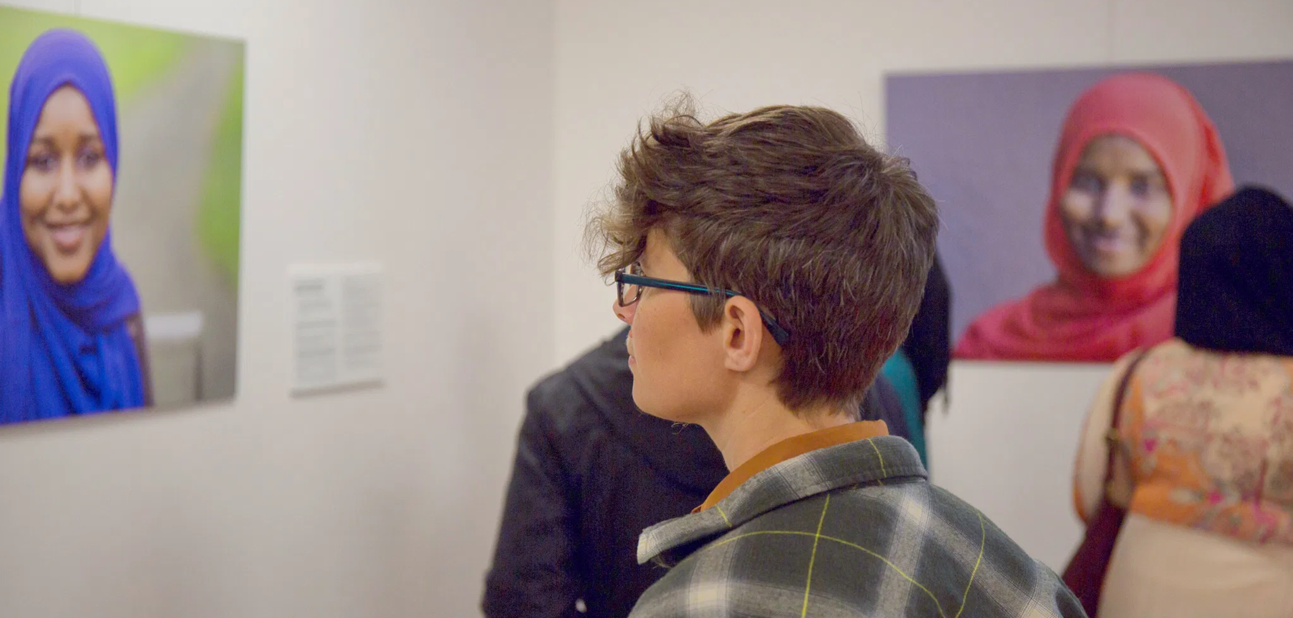 Woman in a museum looking at photo of a woman in a blue hijab.png