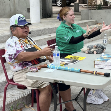 Two people sit at a table speaking to an audience