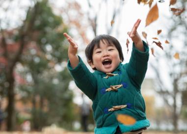 A child with a joyful smile is throwing fall leaves into the air