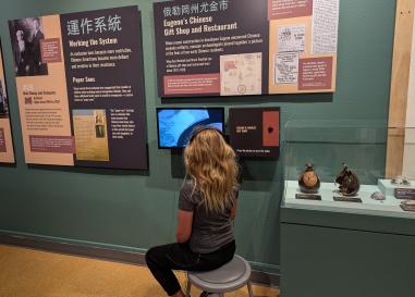 A child sits on a stool and watches a video in Roots and Resilience exhibit