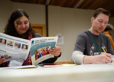 Woman reads pamphlet next to a man writing.