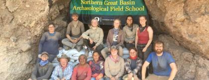 Group of people sit in front of a rock wall with a sign for Field School.