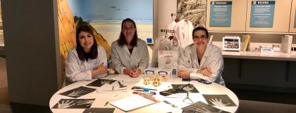Three students in lab coats sitting around a table in the museum