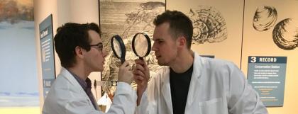 UO students pose in lab coats with magnifying glasses.