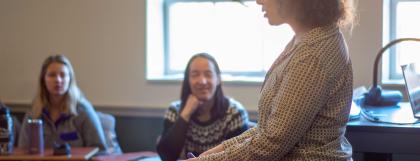 A young person talks to UO students, gesturing at a fossil