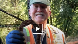 A smiling man in a high-viz vest holds up a rusty horseshoe